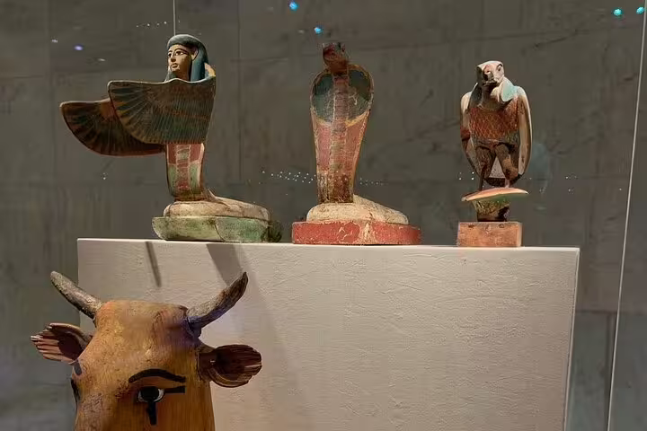 Ancient Egyptian funerary statues and falcon figure in museum case, featured on NMEC and Egyptian Museum guided tour