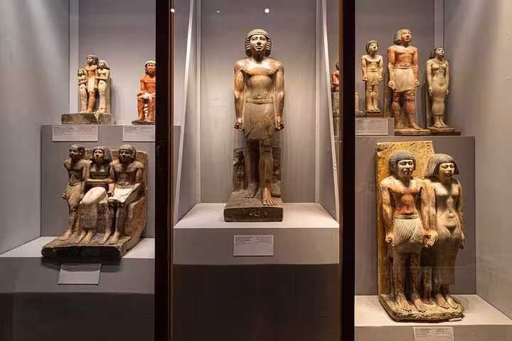 Ancient Egyptian statues and figurines displayed in museum cases at the Grand Egyptian Museum on a VIP Cairo tour