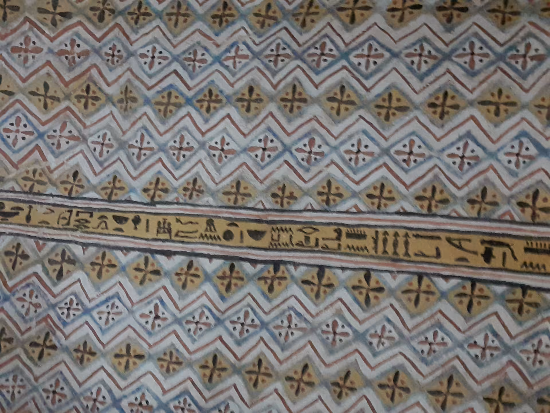 Intricate Egyptian wall painting with colorful geometric patterns and hieroglyphs at an ancient site.