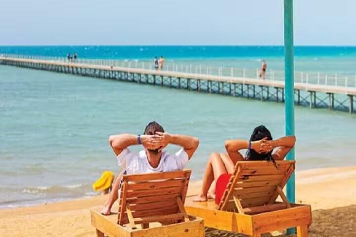 Couple relaxing on beach loungers by the Red Sea during El Ain El Sokhna day trip from Cairo with pier view
