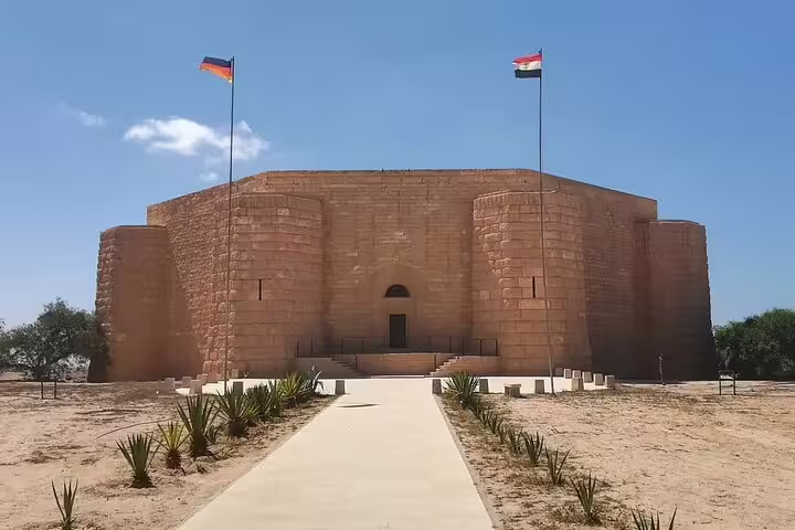 El Alamein War Museum exterior with flags and desert walkway, private day tour from Cairo to El Alamein and Alexandria