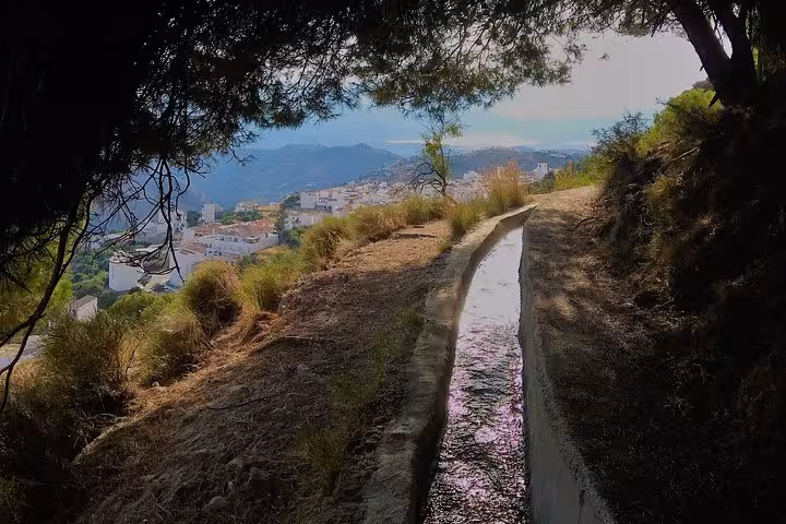 Scenic view of a hiking path and white village in El Saltillo Gorge near Malaga, surrounded by lush greenery.