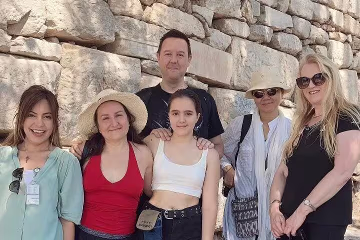 Group of tourists enjoying the Ephesus tour, posing against ancient stone walls under sunny skies.