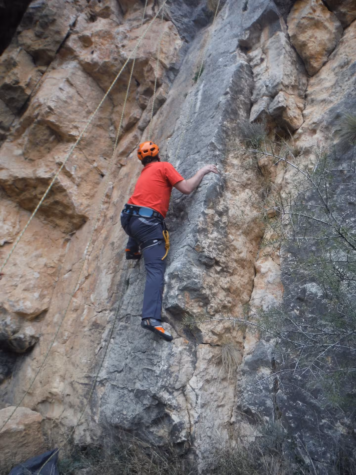 Escalador principiante con casco naranja sube pared de roca con cuerda y arnés en actividad de escalada guiada