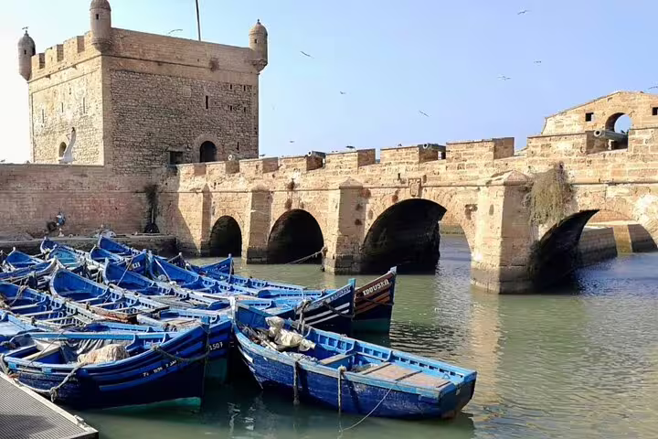 Blue fishing boats at Essaouira harbor and historic ramparts, coastal day on Morocco 12 days tour from Marrakech