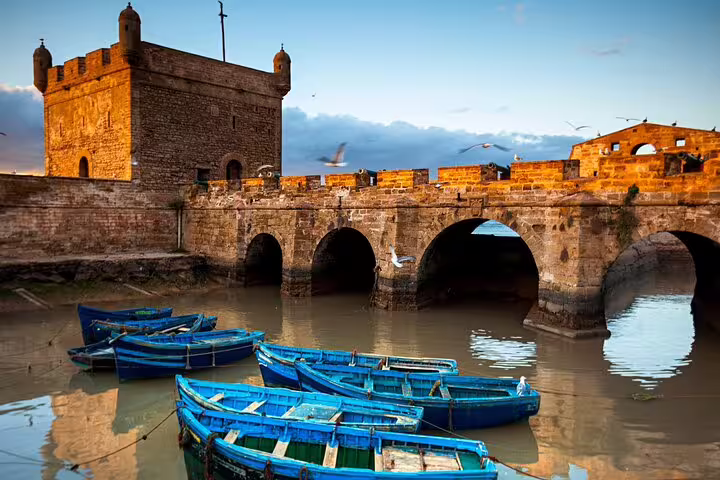 Essaouira port ramparts and stone bridge with blue fishing boats, Morocco 11 days tour from Marrakech