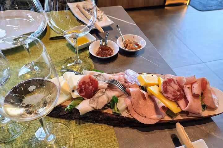 A gourmet charcuterie board with assorted meats, cheeses, and wine glasses offers a taste of Sicilian flavors at Etna winery.