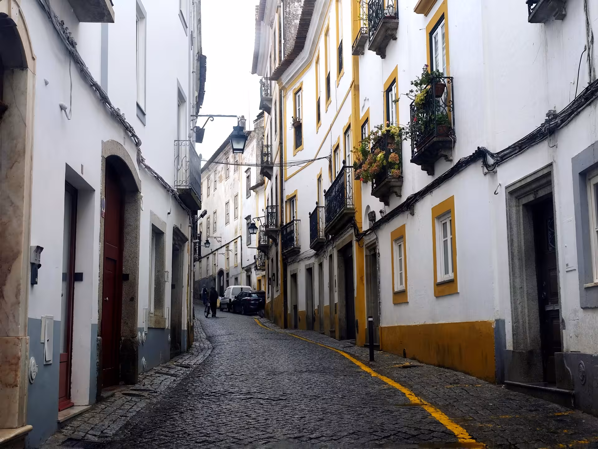 Narrow cobblestone street with white-and-yellow houses and balconies in Évora historic center walking tour