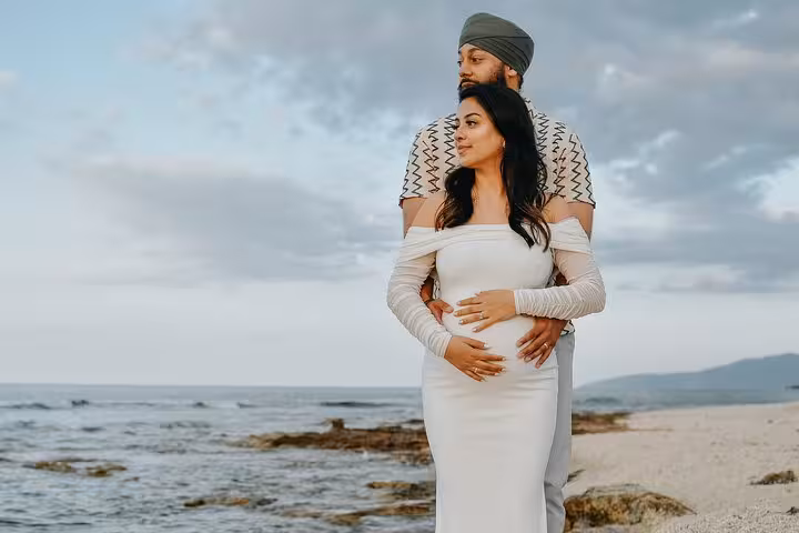 Expectant couple embracing by Heraklion beach for a serene pregnancy photoshoot with ocean backdrop.