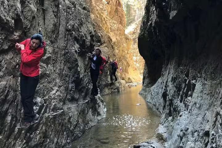 Hikers traversing narrow canyon walls on rope cables above a mountain stream in Fagaras