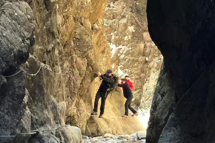Two hikers navigating a narrow rocky cliff ledge using safety ropes in Fagaras Mountains