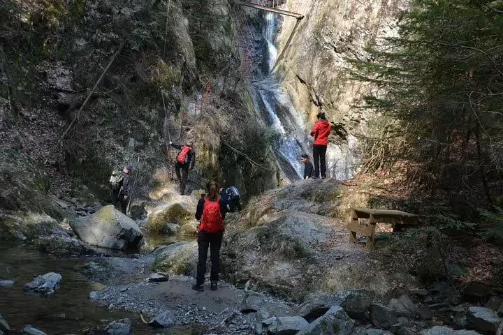 Hikers with red backpacks exploring a rocky gorge with waterfall on Fagaras hiking tour