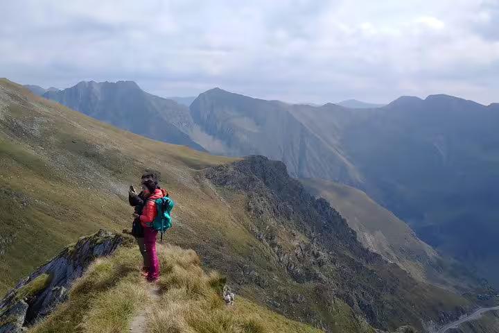 Hiker with backpack standing on Fagaras Mountain ridge overlooking dramatic Romanian mountain valley