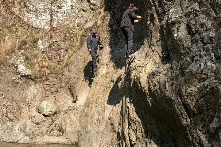 Two hikers climbing rocky cliff face on Fagaras mountain trail with metal ladder and iron rungs