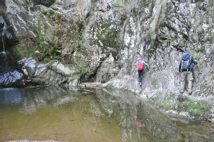 Two hikers climbing rocky gorge trail beside a tranquil mountain pool in Fagaras mountains, Romania