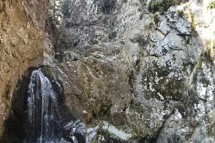 Waterfall cascading down rocky canyon cliffs with metal ladder on Fagaras hiking trail