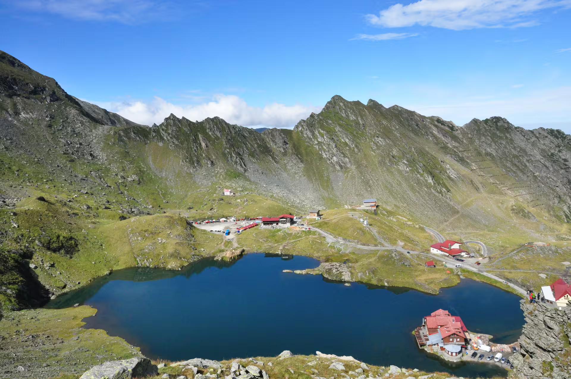 Glacial Balea Lake surrounded by rocky Fagaras Mountains peaks with mountain chalets on the shore
