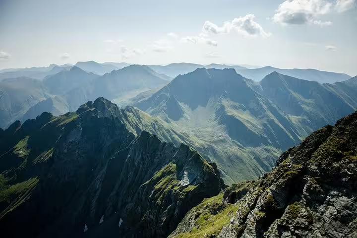 Panoramic view of Fagaras Mountains peaks and green valleys from a rocky summit in Romania