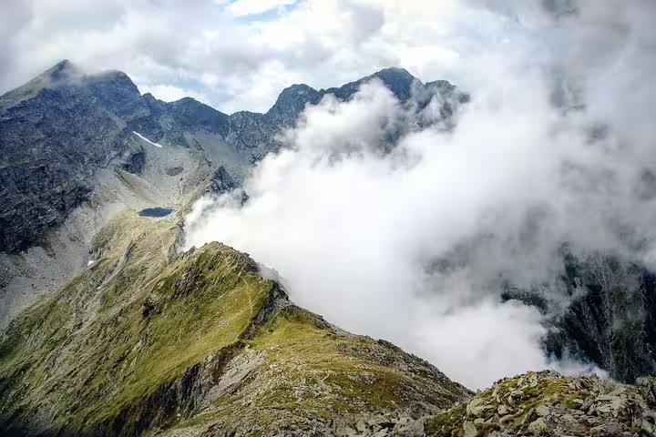Rocky Fagaras mountain ridge with alpine lake and low clouds rolling over peaks in Romania