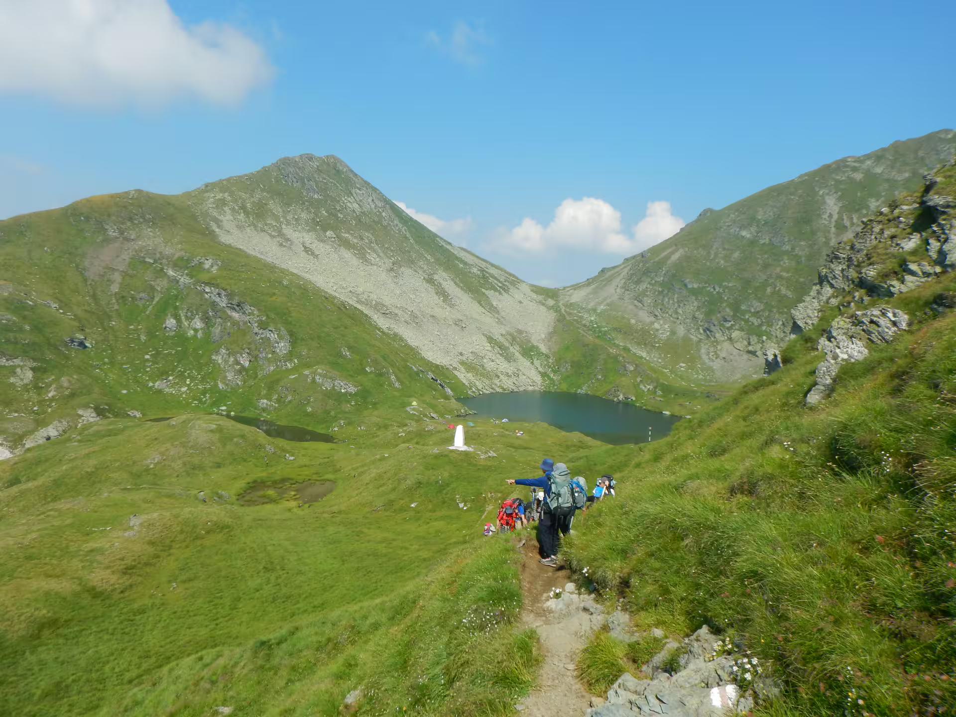 Hikers trekking down mountain trail toward alpine lake in Fagaras Mountains, Romania