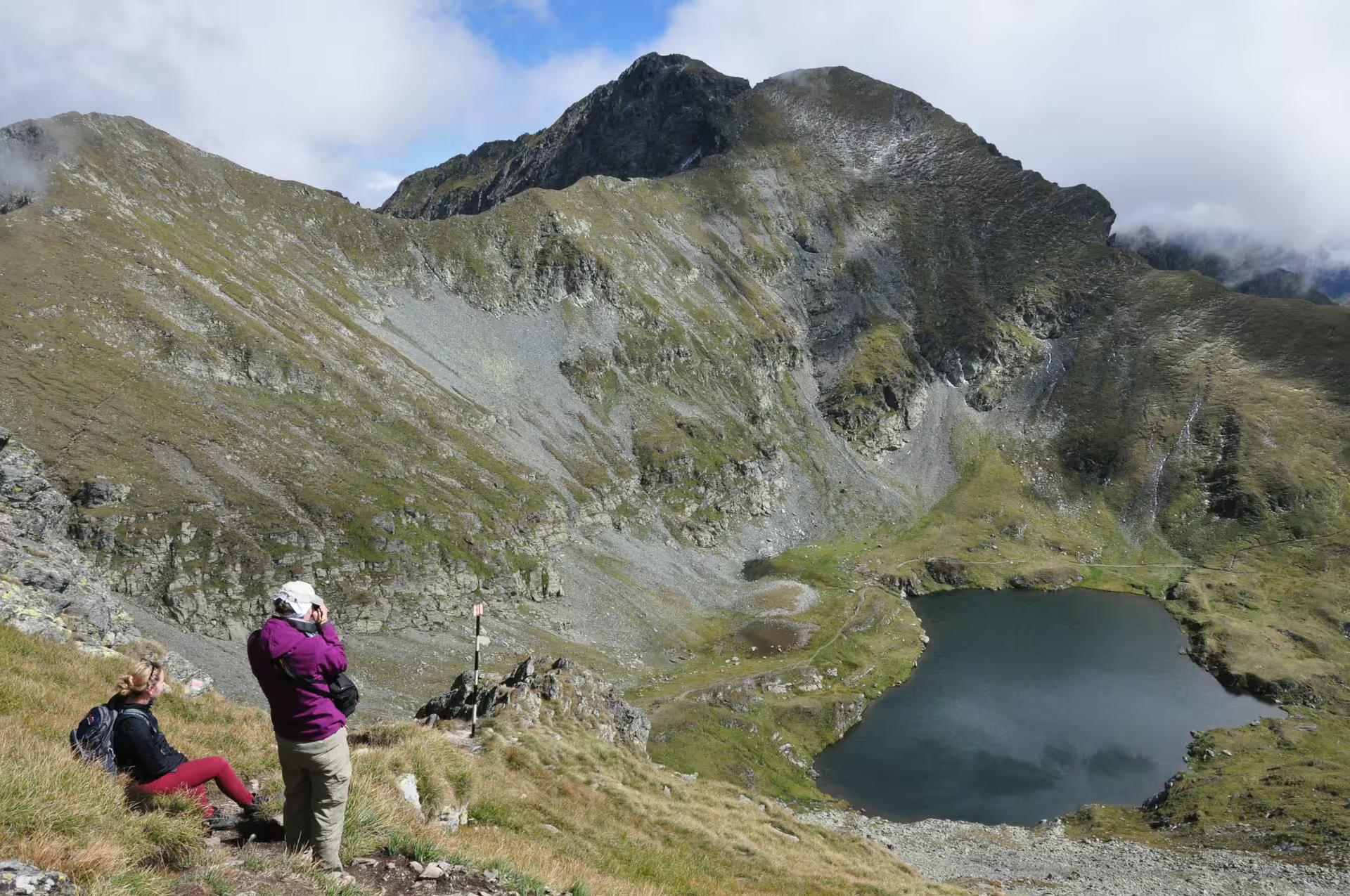 Two hikers overlooking a glacial lake and rocky Fagaras Mountains peaks in Transylvania, Romania