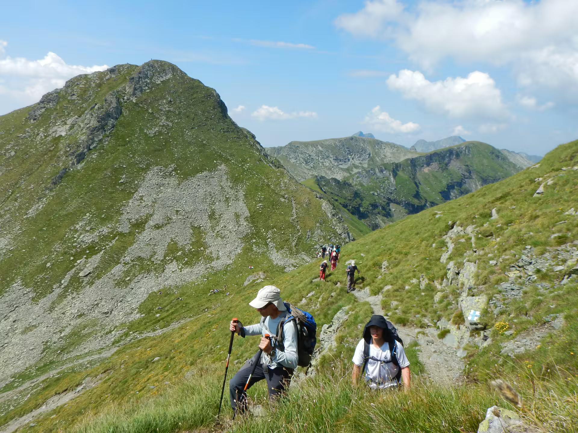 Hikers trekking up a mountain ridge trail in the Fagaras Mountains with peaks in background