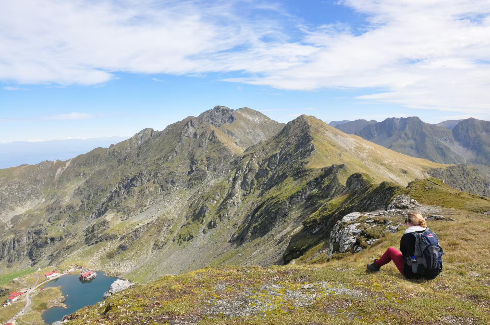 Hiker resting on Fagaras Mountains ridge overlooking glacial lake and rocky peaks near Brasov