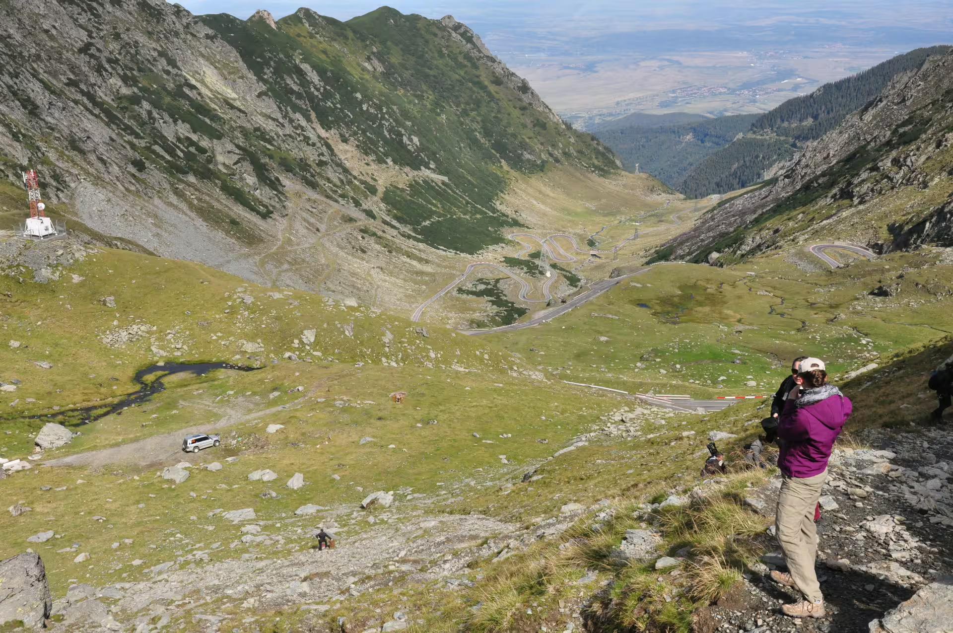 Hiker photographing the winding Transfagarasan road through Fagaras Mountains valley from Brasov