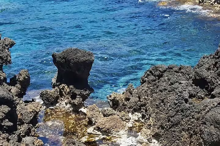 Crystal-clear blue waters meet rugged volcanic rocks at Falassarna Beach on a scenic tour from Chania.