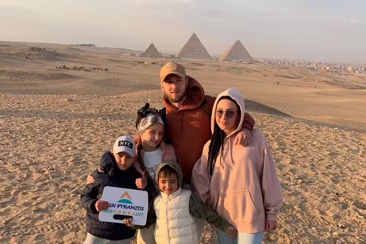 Family photo at Giza Plateau with pyramids backdrop on a Cairo day trip from Alexandria with transfers