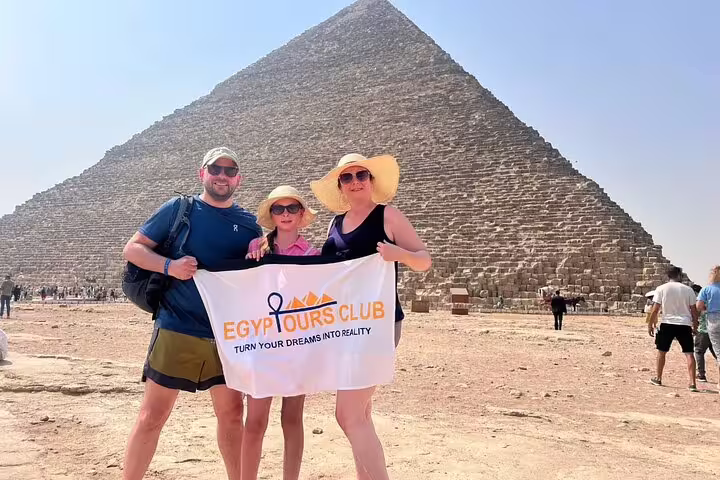 Family posing with tour banner at the Great Pyramid of Giza on a private Cairo tour to Saqqara and Memphis