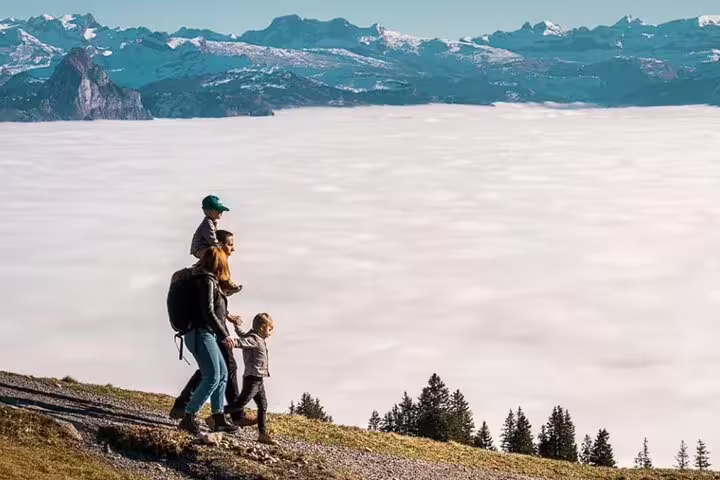 Family hiking on Mount Rigi with stunning cloud-filled valley and snow-capped peaks in the background.