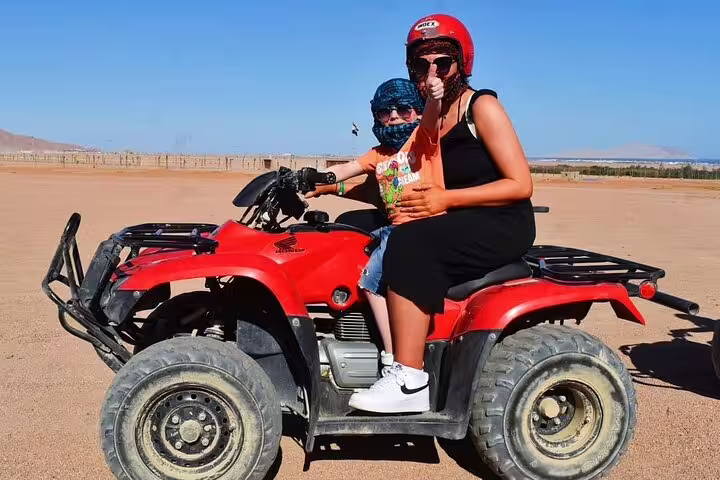 Family riding red ATV quad bike in Sinai Desert on Sharm El Sheikh safari adventure tour, wearing helmets