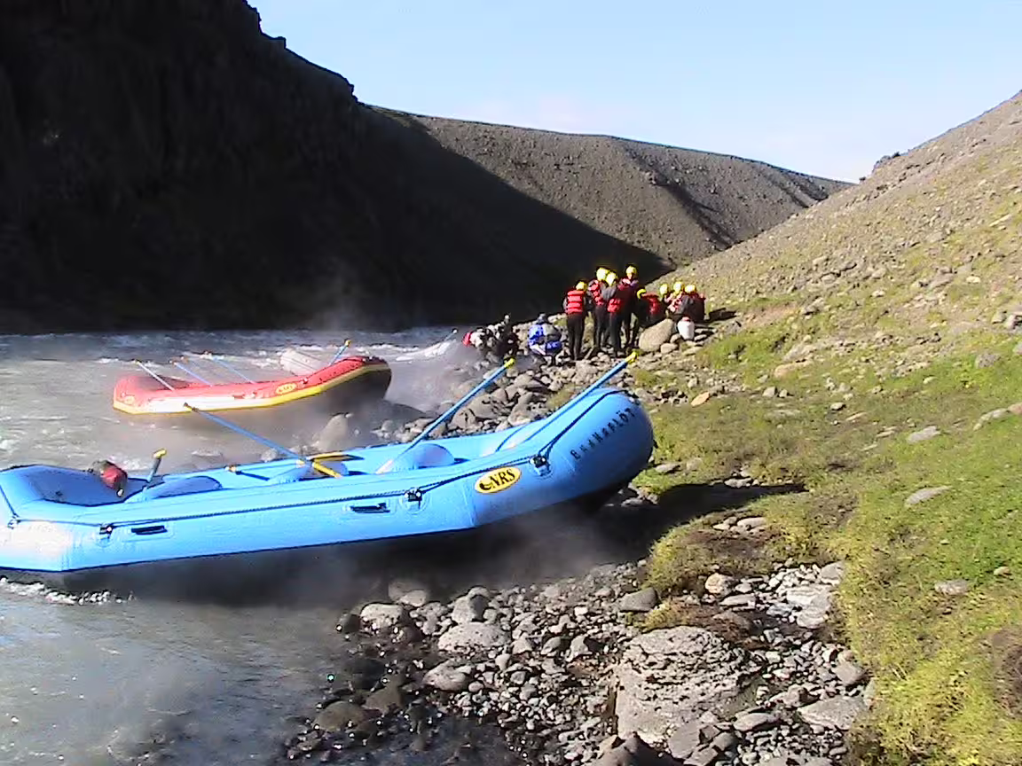Blue and red rafts on a rocky riverside with people in helmets and life jackets preparing for an exciting family river rafting adventure.