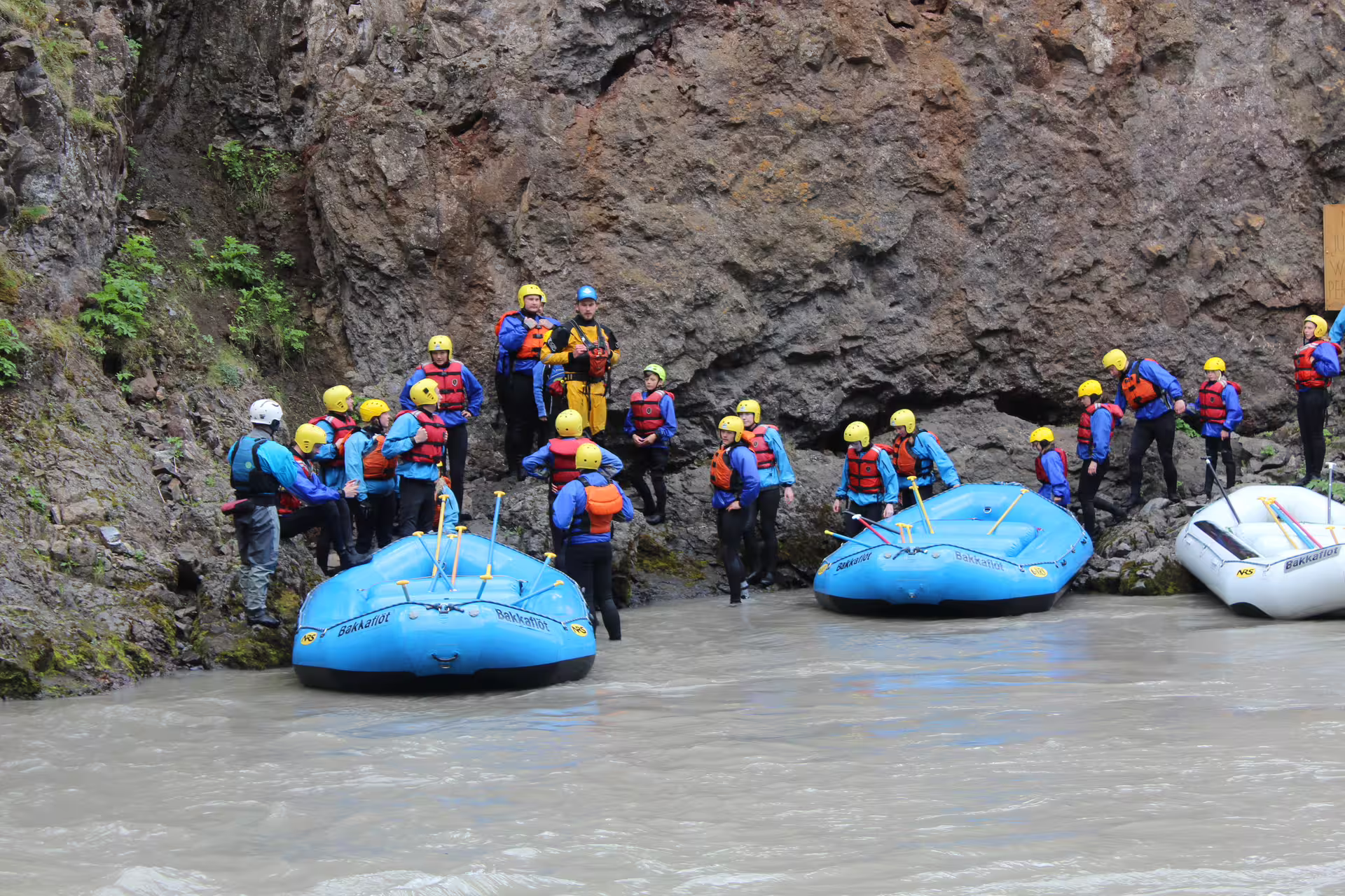 Family river rafting adventure with group in safety gear preparing on rocky shore, perfect for outdoor family fun and bonding.