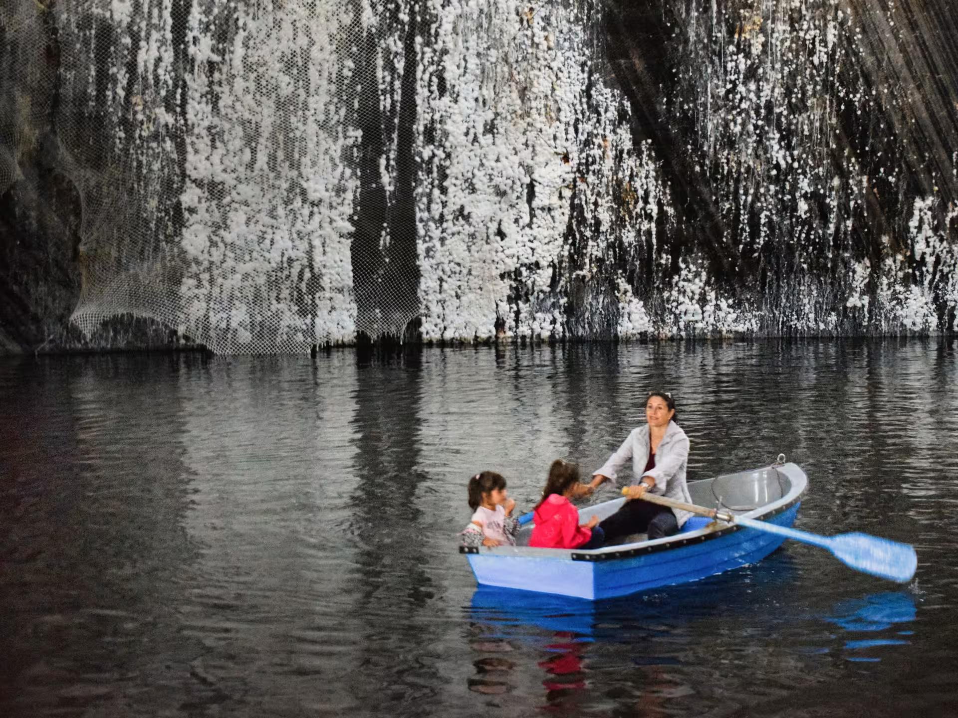 Family rowing a blue boat on the underground lake inside Turda Salt Mine during a guided tour from Cluj Romania