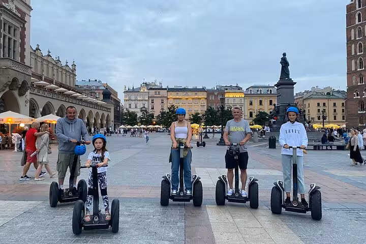Family on a Segway tour in Krakow's main square, experiencing the charm of the Jewish Quarter at dusk.