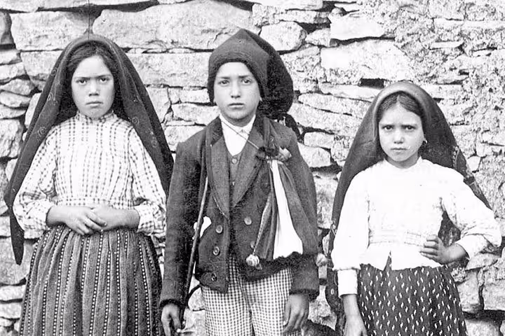 Three children in traditional attire stand solemnly against a stone wall, capturing the historical essence of Fatima's past.