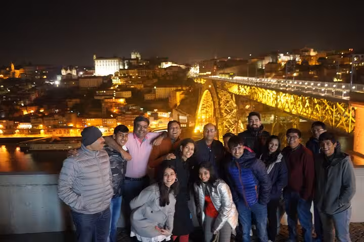 Travel group photo with illuminated Porto skyline and Dom Luís I Bridge, add-on stop on Fátima Santiago Nazaré tour