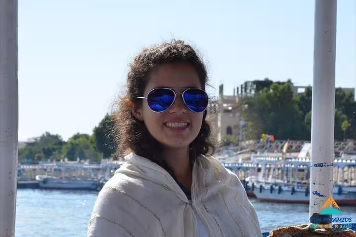 Traveler smiling on a felucca boat in Luxor, enjoying a Nile River sailing tour with scenic riverbank views