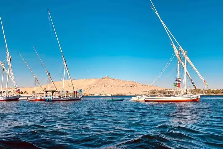 Traditional felucca sailboats cruising the Nile in Luxor with desert hills, scenic private felucca ride