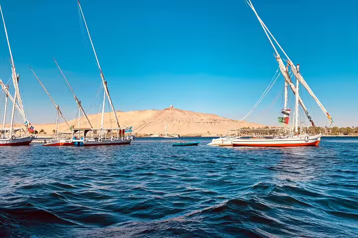 Traditional felucca sailboats on the Nile in Luxor with desert hills, classic sunset sailing tour in Egypt