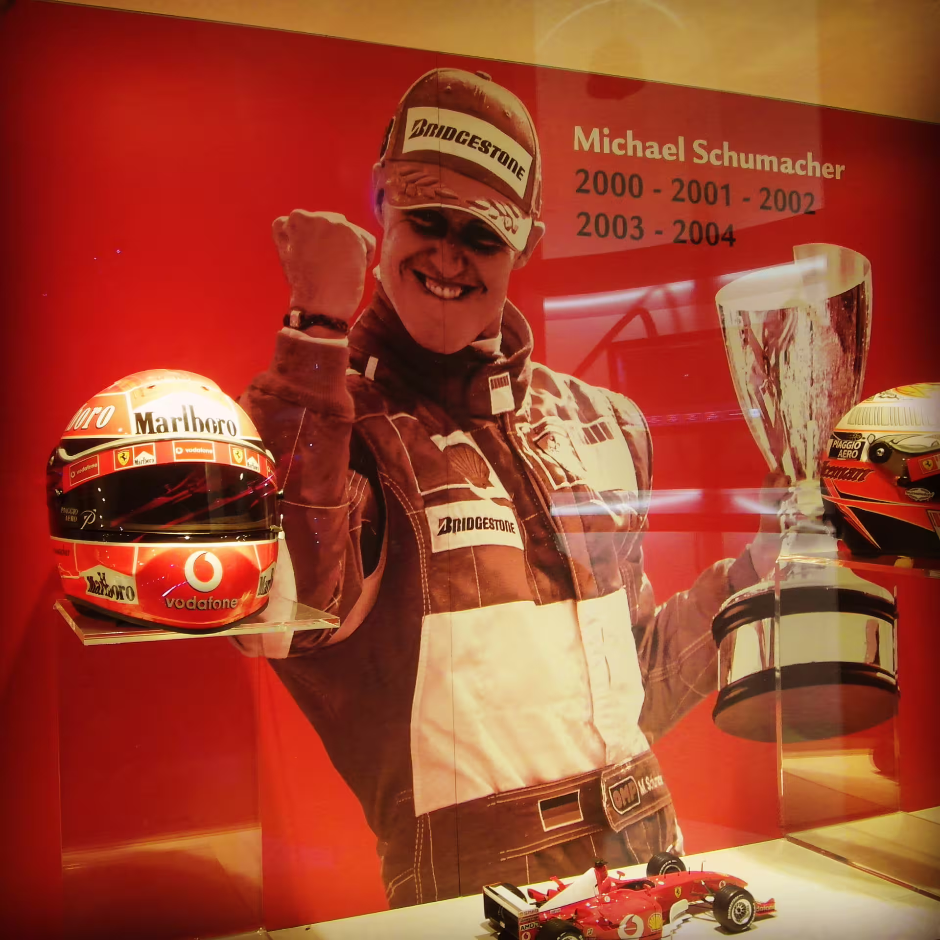 Exhibit honoring a famous Formula 1 champion with helmet, trophy, and memorabilia at Ferrari Museum.