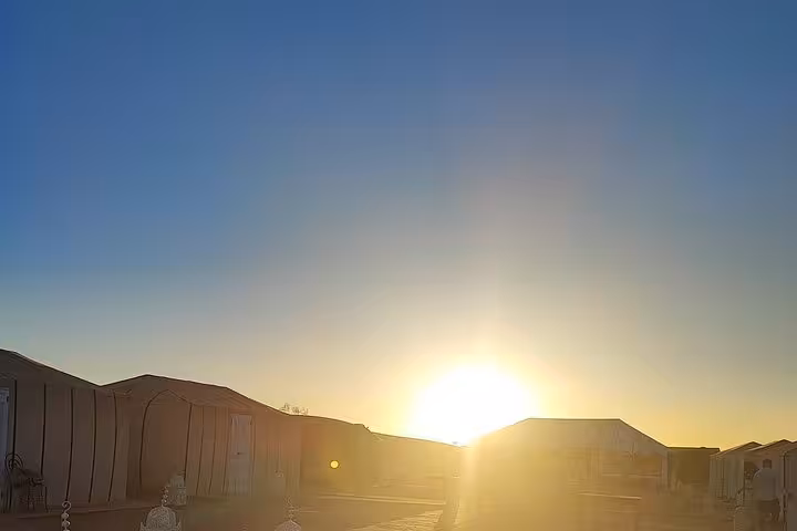 Golden sunrise over desert tents in Merzouga, offering a serene start to the 4-day Fes to Marrakech group tour.