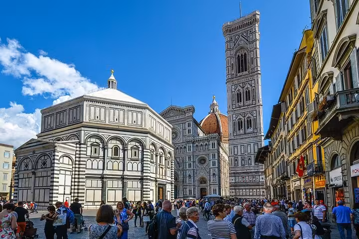 Crowded Piazza del Duomo in Florence featuring the iconic Cathedral and Bell Tower under a clear blue sky.