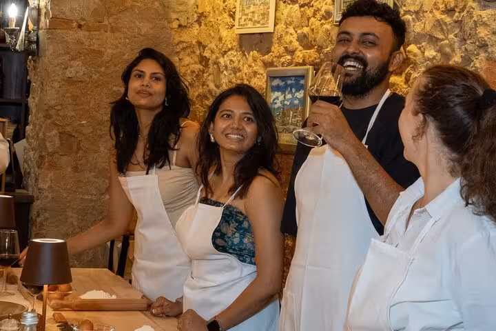 Group enjoying Florence cooking class, wearing aprons and savoring wine in a rustic setting.