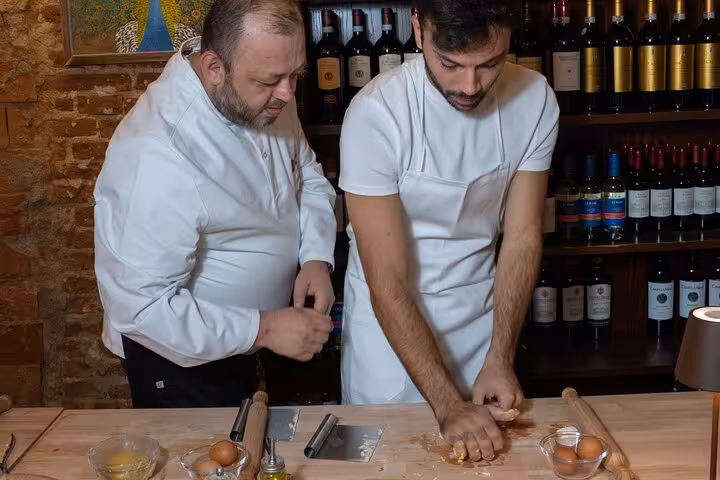 Chef instructing a participant in pasta-making technique during a hands-on cooking class in Florence.