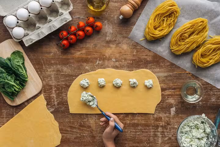 Hand placing ricotta filling on pasta sheet surrounded by fresh ingredients at Florence cooking class.