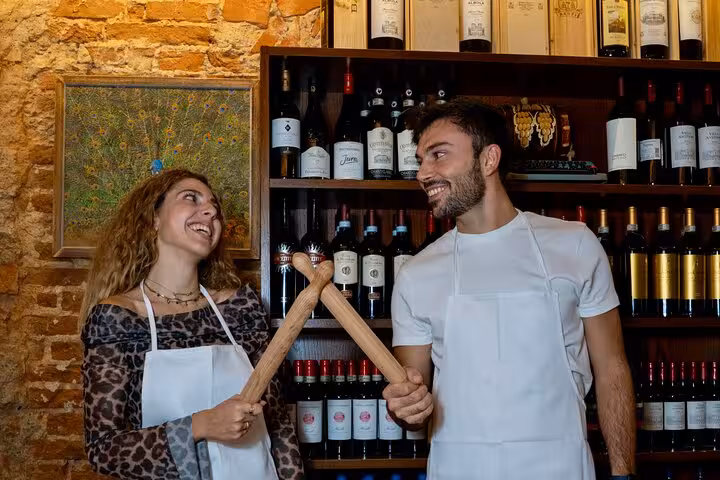Two participants joyfully clinking rolling pins during a pasta and tiramisu cooking class in Florence.