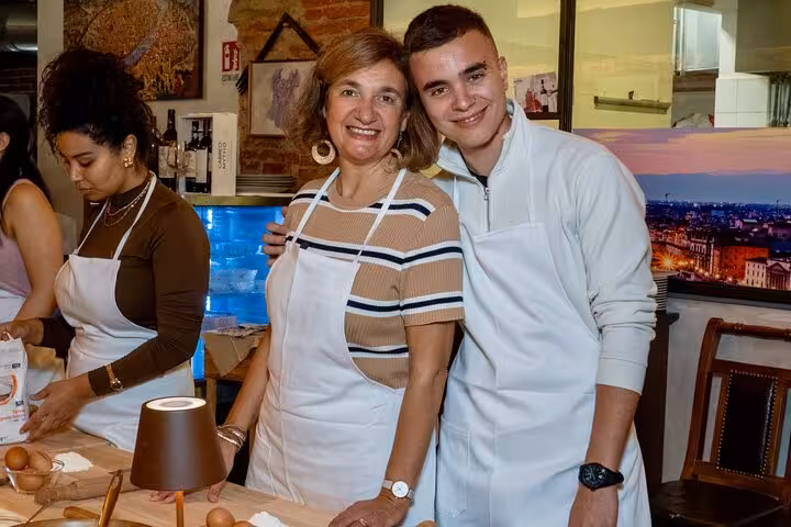 Smiling participants in aprons at a Florence pasta and tiramisu cooking class enjoying unlimited wine.